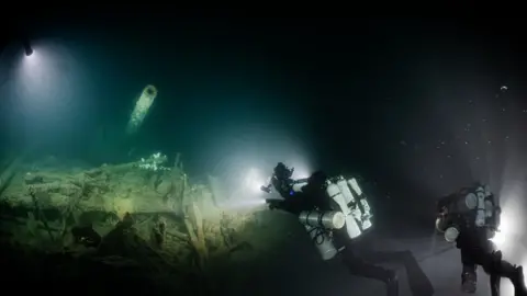 Steffen Scholz Divers shine a light on a gun turret, part of the wreckage of a Royal Navy warship. 