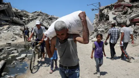 Reuters A Palestinian man carries a bag with aid supplies that entered Gaza, in Beit Lahia, northern Gaza (27 July 2025)