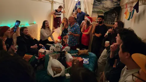 James Chater/BBC A group of people stand around a pile of presents