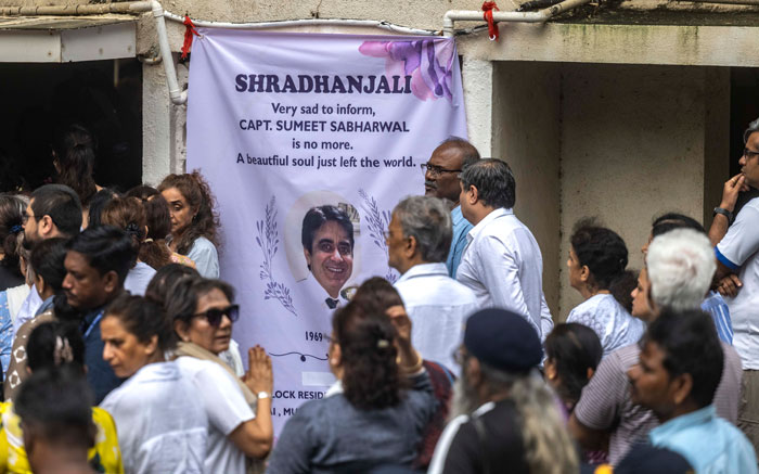 Mourners gathered at a memorial banner for Air India pilot Capt Sumeet Sabharwal amid personal turmoil and crash investigation.