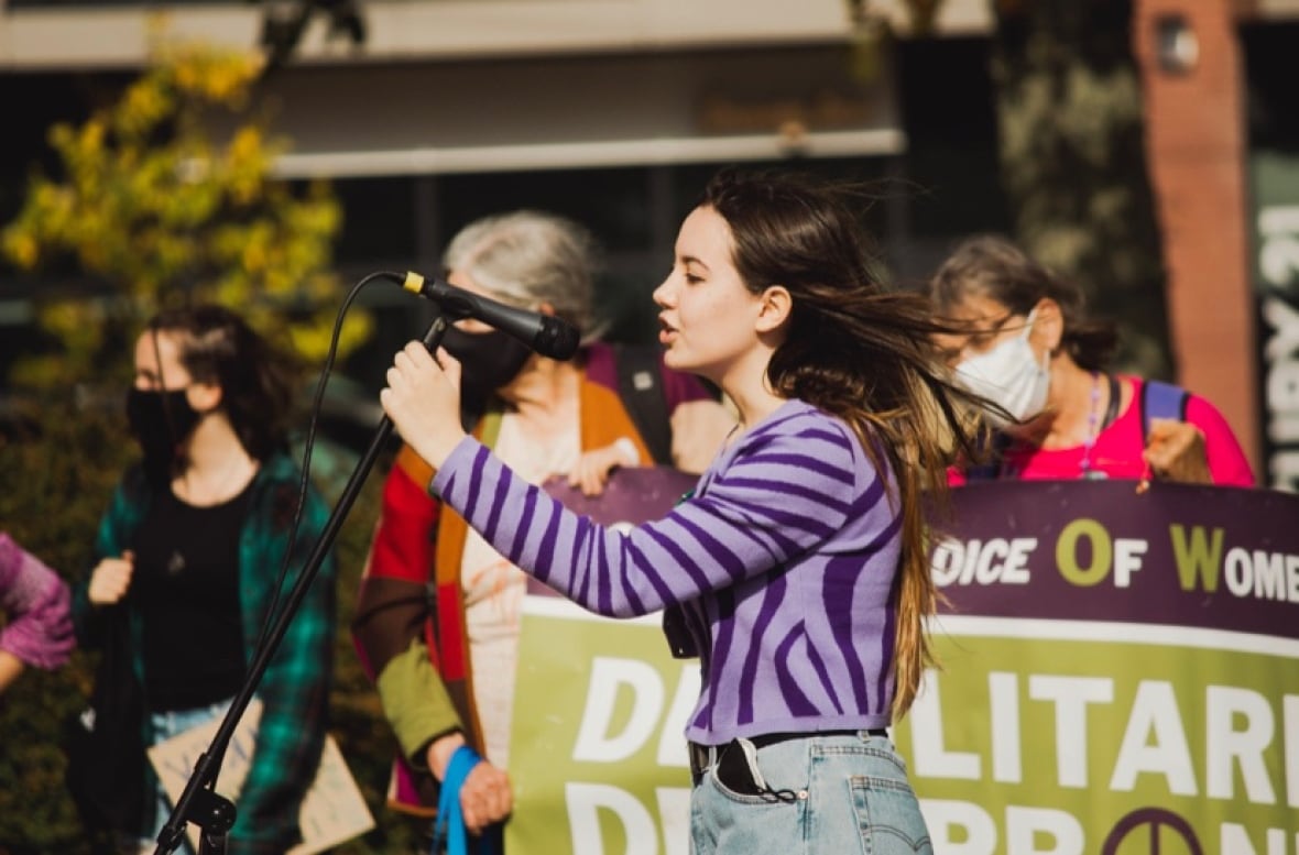 A teenage girl speaks into a microphone at a rally.