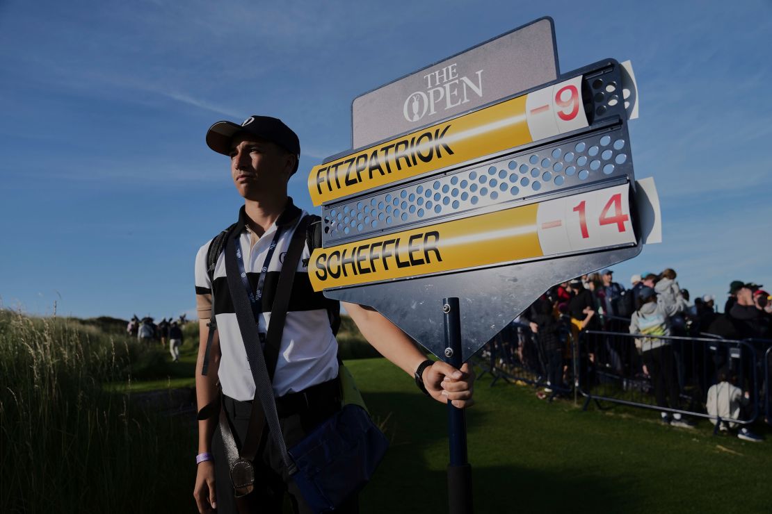 A scoreboard operator shows the score of Scheffler and Matt Fitzpatrick of England going to the 18th hole.