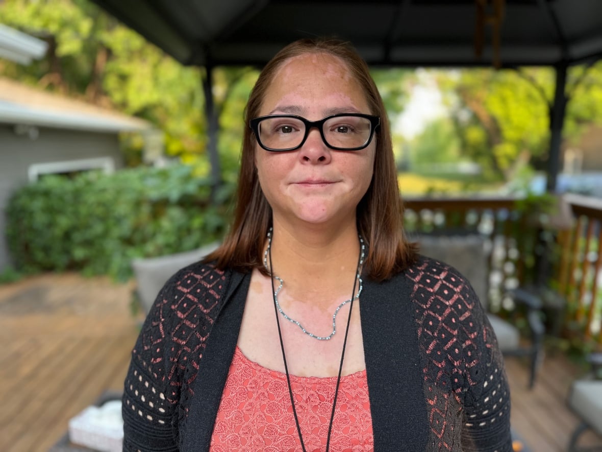 Woman with glasses stands on a back deck.