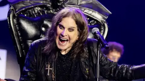 Ross Halfin Ozzy Osbourne, dressed in a black leather jacked sat on a black throne with a microphone in front of him