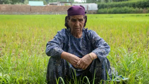 Faisal Bashir A woman sitting in a field wearing a blue top and a purple scarf