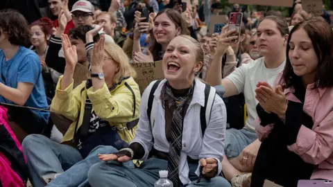 TETIANA DZHAFAROVA/AFP Young Ukrainians sit outside parliament clapping and holding placards