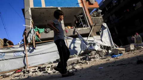 Reuters A Palestinian boy walks near a UNRWA school sheltering displaced people that was hit in an Israeli strike, in Gaza City (5 July 2025)