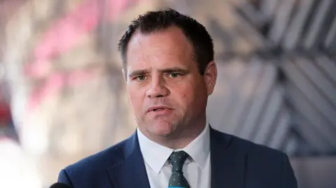 Getty Images Irish Minister of State Neale Richmond, with short brown hair, wearing a navy suit, white shirt and dark green tie. The background of the image is blurred. 