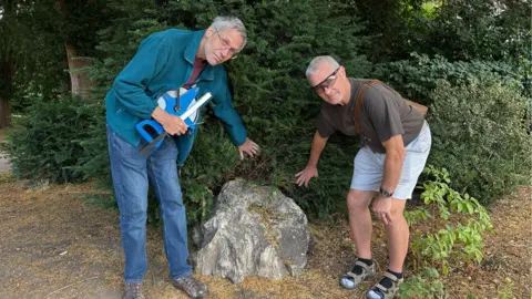 BBC Two men standing next to a fossilised tree stump in Markeaton Park, Derby.