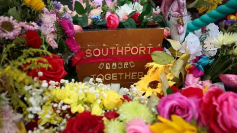 PA Media Flowers which have been left by members of the public are seen following the fatal knife attack in Southport. In the middle is a sign which reads: "Southport stands together".