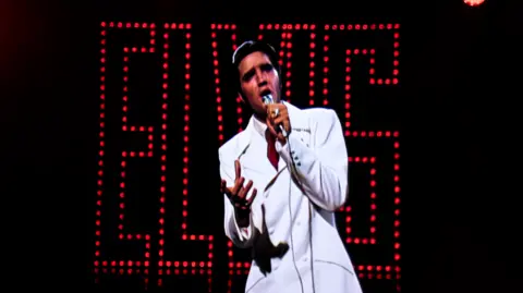 Graham Turner Elvis Presley in a white suit and a microphone in one hand