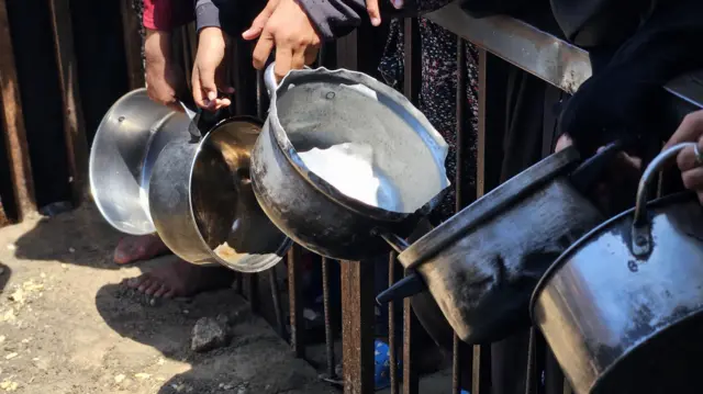 Hands holding cooking pots by a fence