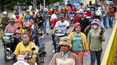 Getty Images Garment workers, men and women, walk out in a large group from their factory during their lunch break in Phnom Penh on July 8, 2025.