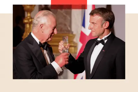 Getty Images Macron and King Charles toast glasses, while looking happy and wearing black tie outfits