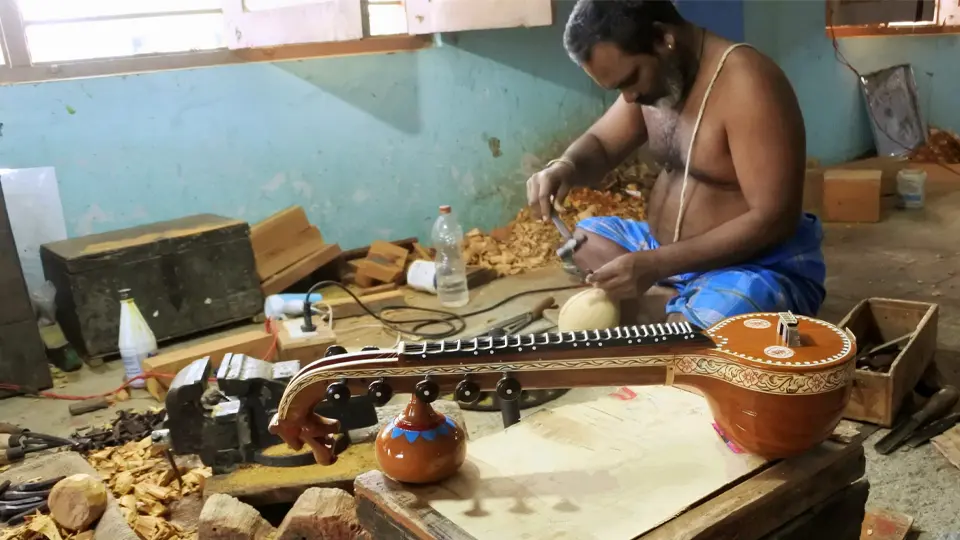 Craftsman working in a workshop, shaping a miniature Bobbili veena; a finished one lies in the foreground.