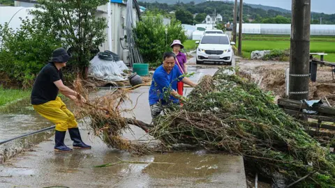 Getty Images Villagers pull up branches and debris swept from the flood in Gansan-Myeon, South Chungcheong Province, South Korea, on July 17, 2025. 