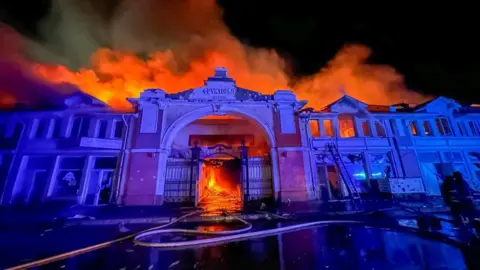 DSNS Odesa The facade of Odesa's market at nighttime, with a fire raging behind it