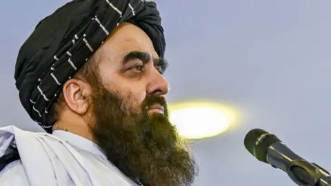 Getty Images Afghanistan's Foreign Minister Amir Khan Muttaqi, with a long black beard, is in profile with a microphone directly in front of him. 