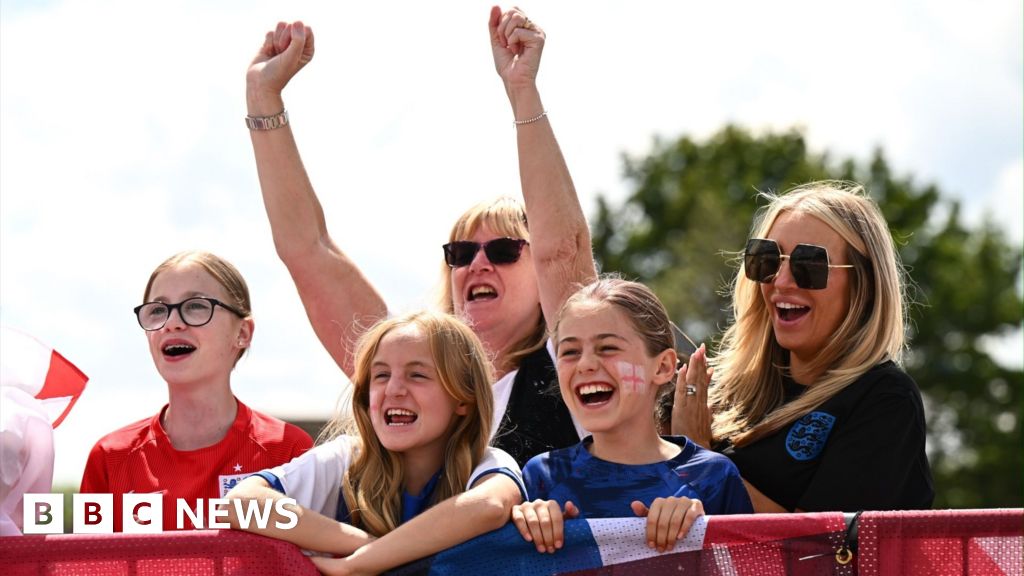 Five England fans smile at Southend Airport, waiting for the Lionesses to arrive home