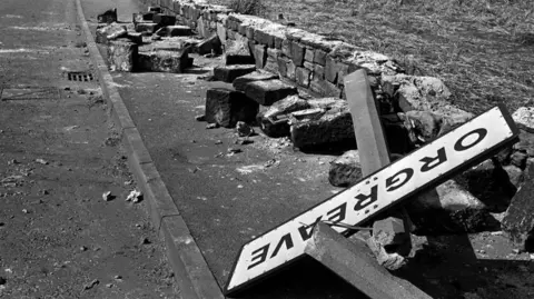 PA Media A black and white image of a twisted sign, felled concrete posts and a broken wall following violence outside the coking plant in Orgreave, South Yorkshire.