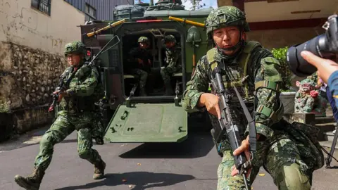 Getty Images Two Taiwanese soldiers leap out of a military vehicle while holding rifles in a military exercise in Taichung