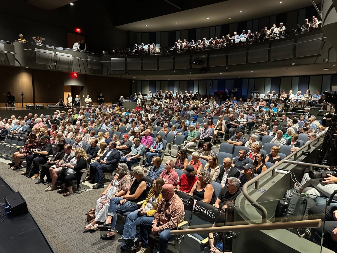 A large auditorium, mostly full of people. 