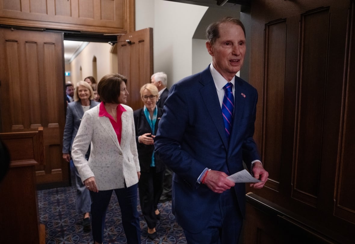 A group of people in business attire walk through a wooden door frame.