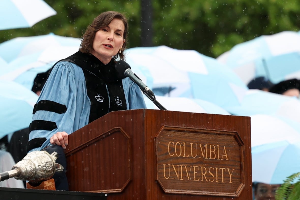 Woman with dark hair, wearing a blue academic robe, speaking at an outdoor podium with the words Columbia University on it