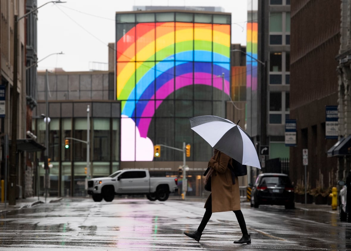 A large rainbow is shown on the National Arts Centre as a woman walks across a quiet street in downtown Ottawa.