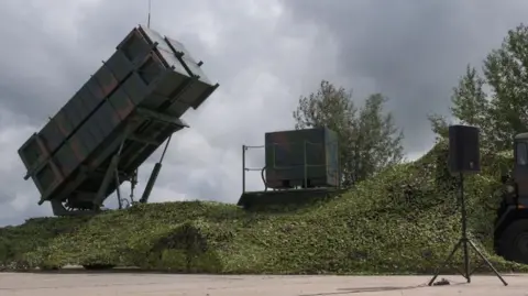 Getty Images A Patriot system received by Ukraine is seen on the Day of Ukrainian Air Force on August 4, 2024 in Ukraine. The camouflage-painted rectangular system is raised at an angle on a platform on top of a grassy mound.