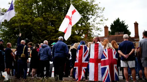 PA Media The backs of a crowd of people. Some are waving St George flags while others have the Union Jack flag wrapped around them.