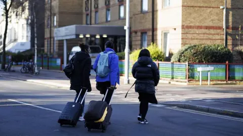 EPA Three asylum seekers wirth luggage move out from a Home Office contracted London hotel