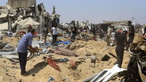 Anadolu via Getty Images People search for belongings after Israeli tanks and bulldozers operated in an area where there was a tent camp, in Khan Younis, southern Gaza (11 July 2025)