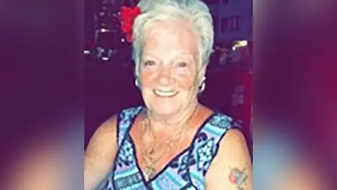 Police handout Sheila Jackson with short white hair wearing a short sleeved blue-patterned top and hoop earrings. She is in a bar smiling.