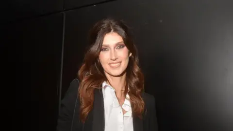 Foc Kan/WireImage via Getty Images Sophie Vouzelaud with long auburn hair and wearing a white short and black jacket in Paris, France, in October 2023.