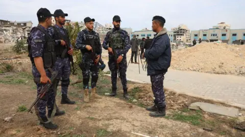 Anadolu via Getty Images Members of the Hamas-run Gaza police force stand next to destroyed buildings at the Arafat Police Academy, in Gaza City, during a ceasefire with Israel (22 January 2025)