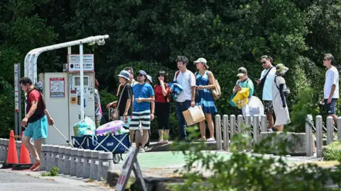 Philip FONG/AFP/Getty Images Holidaymakers in beachwear are seen queuing for a ticket machine to pay for parking as they begin to evacuate a holiday resort in Tokyo Bay. There are trees in the background