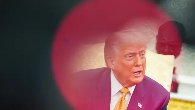 Trump in blue suit with gold tie looks to side, encircled by red flare from camera flash