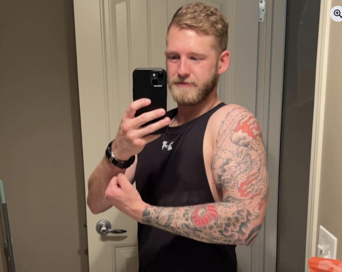 A tattooed man takes a selfie while flexing his arm. 