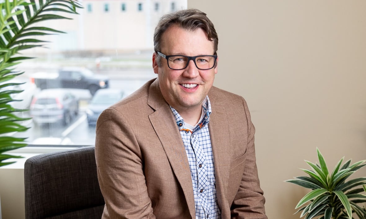 A man sits in a chair in an office with plants visible on either side.