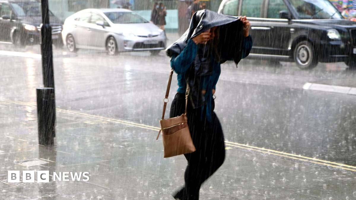 Woman walking in heavy rain holding a jacket over her head.
