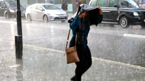 Getty Images Woman walking in heavy rain holding a jacket over her head.