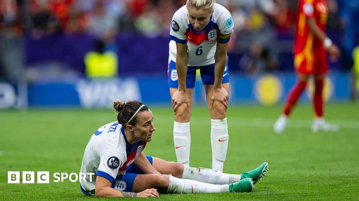 Lucy Bronze of England on the ground during the Euro 2025 final match between England and Spain. Leah Williamson stoops over the defender.