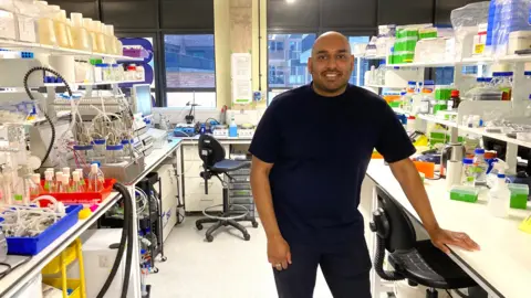 Jevan Nagarajah stands in Better Dairy's lab in east London. He wears a dark top and trousers.