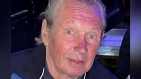 Police handout Peter Eric Greener is smiling. He has short grey hair and is wearing a grey top and blue coat. 