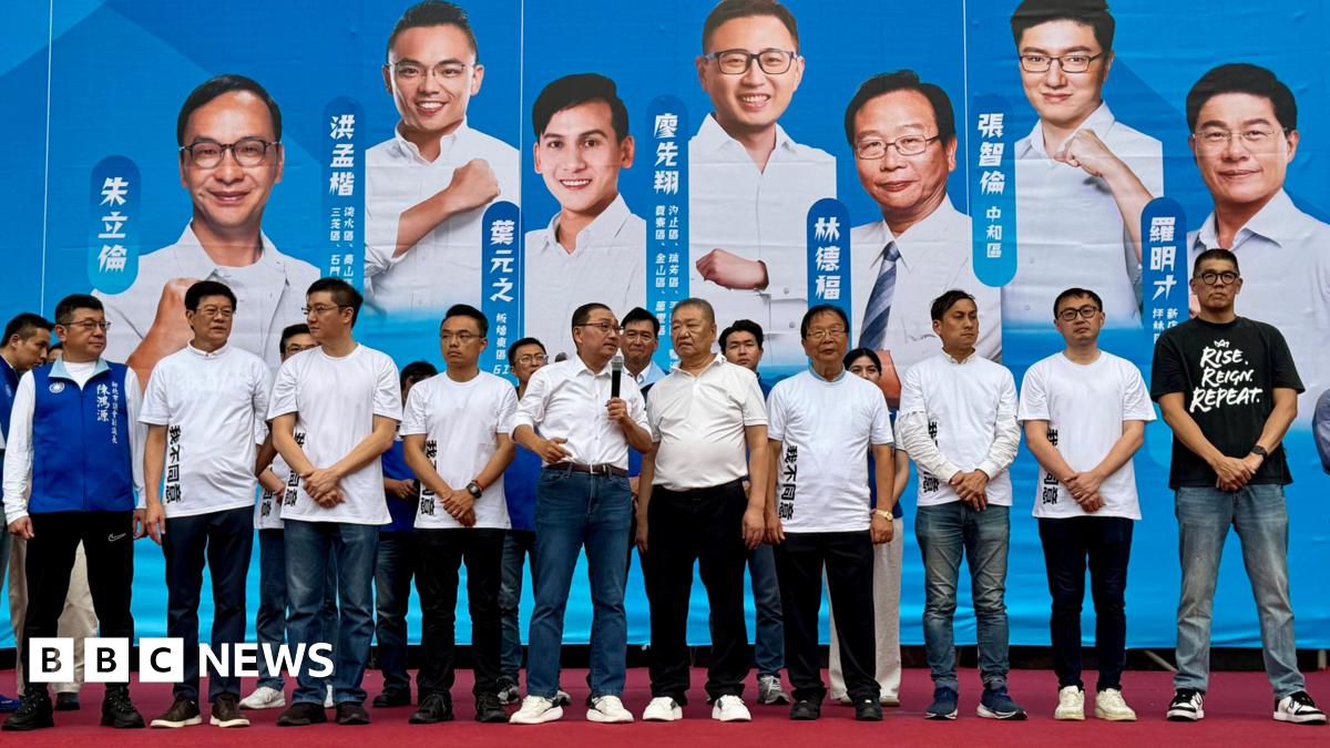 Several Kuomintang lawmakers dressed in white T-shirts and dark trousers stand on stage addressing a crowd at a rally. Behind them is a large blue and white backdrop showing campaign photos of the lawmakers.