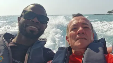 Albert Alfonso/Flickr Yostin Mosquera (Left) and Albert Alfonso (right) on a speedboat. They are wearing lifejackets and smiling at the camera. There is clear blue sea behind them with the wake of the waves. In the distance palm trees can be seen on the shore line. 