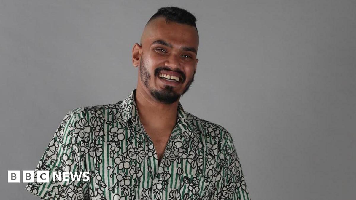 Mohaimon with a big smile looking at the camera, wearing a cotton printed shirt which is both striped and has flower images on it.
