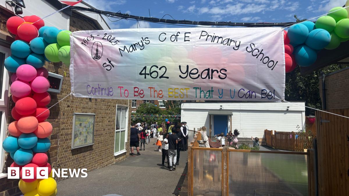 A bright banner at St. Mary's C of E Primary School celebrating 462 years with the message, "Continue To Be The BEST That U Can Be!". Colorful balloons decorate the banner and people are gathered in the background.