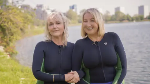 WWF Actors Miranda Richardson and Maggie Service are wearing black and green matching swimming costumes that cover their arms. They are standing in front of a river. 